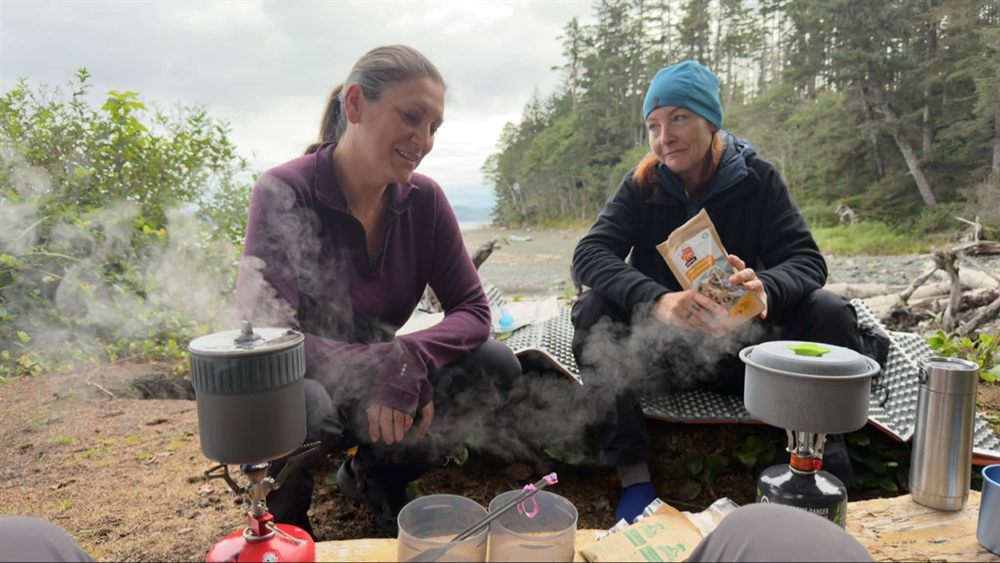Amanda and a friend cooking breakfast on camp stoves at a beach campsite on the North Coast Trail