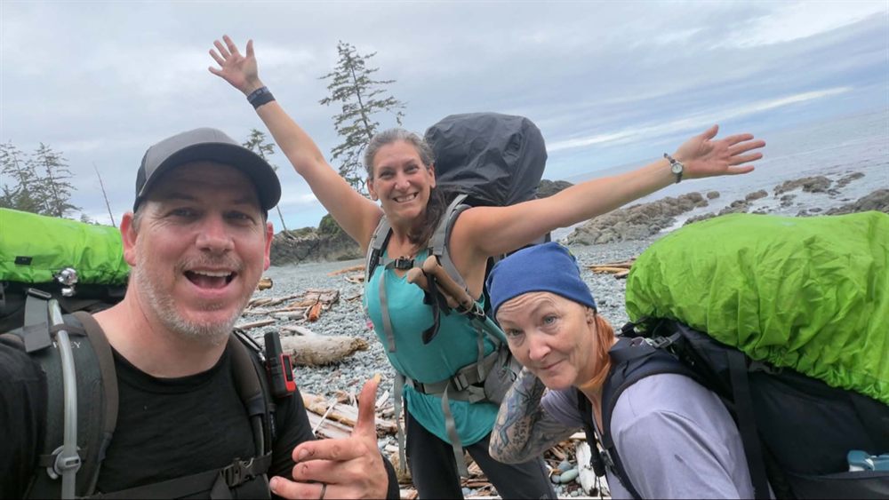 Amanda and two hiking friends cheering on a rocky beach on the North Coast Trail