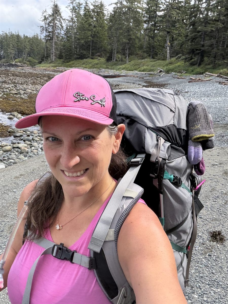 Amanda Robinson in a pink cap with a full backpack on a rocky West Coast beach