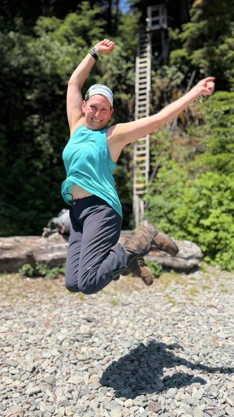 Amanda jumping for joy in front of a tall wooden ladder on the West Coast Trail