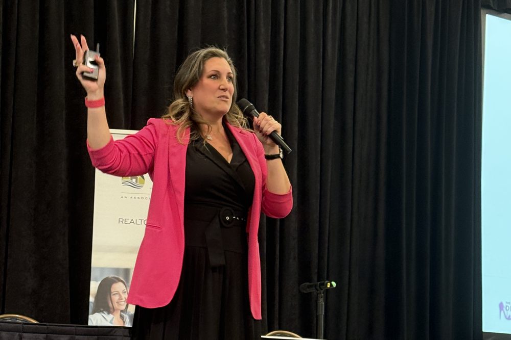 Amanda presenting on stage in a pink blazer at a Vancouver Island Real Estate Board event